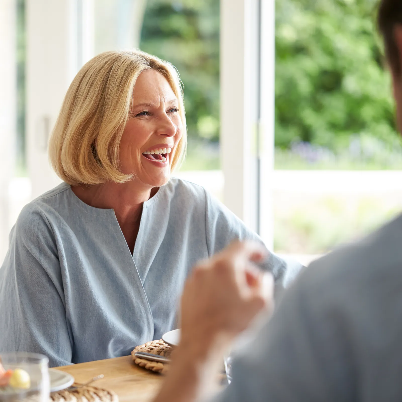 A smiling older woman chatting with someone over a meal at home
